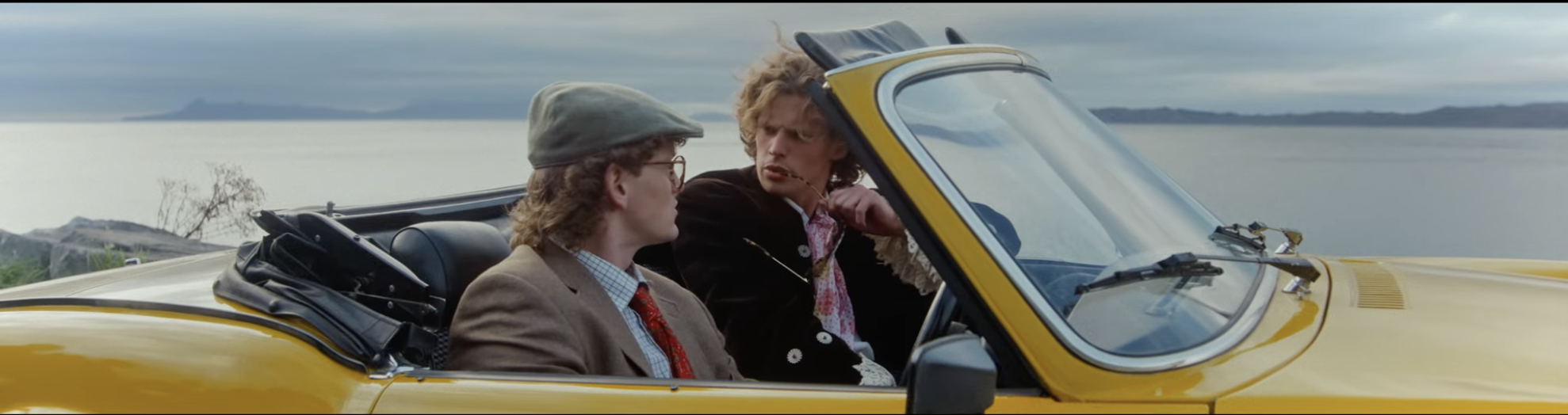 Film still — two figures in a yellow convertible by the coast